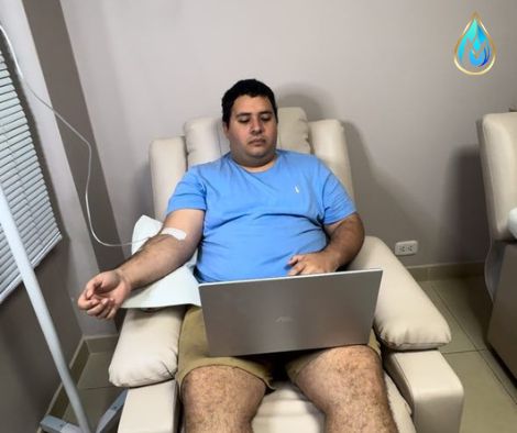 Tratamiento endovenoso Cocktail de Suplementos Naturales para relajación y bienestar, paciente tranquilo y cómodo en sillón trabajando virtual